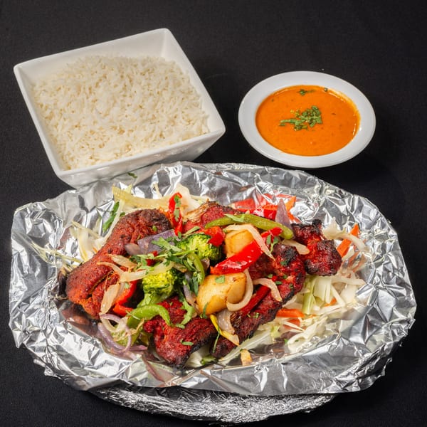 Saffron Indian Cuisine's Tandoori Chicken with vegetables, rice, and a side of orange sauce.