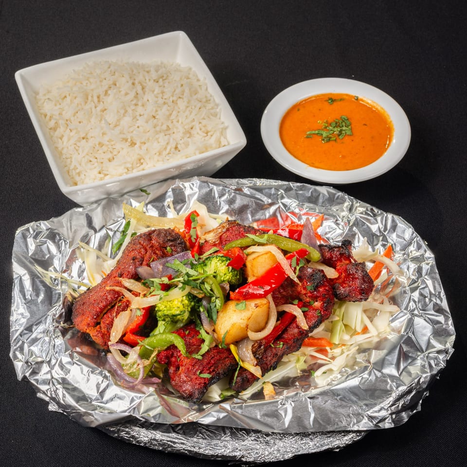 Saffron Indian Cuisine's Tandoori Chicken with vegetables, rice, and a side of orange sauce.