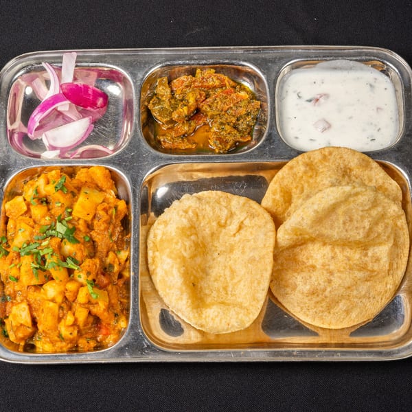 Saffron Indian Cuisine's thali with puri, potato curry, pickle, raita, and red onion slices.