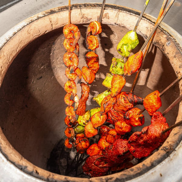 Skewers of shrimp, chicken, and vegetables cooking inside a traditional Indian tandoor oven.