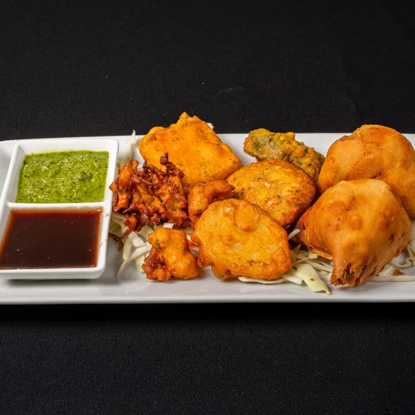 A platter of Saffron Indian Cuisine's fried appetizers, including samosas, pakoras, and bhajis, with two dipping sauces.