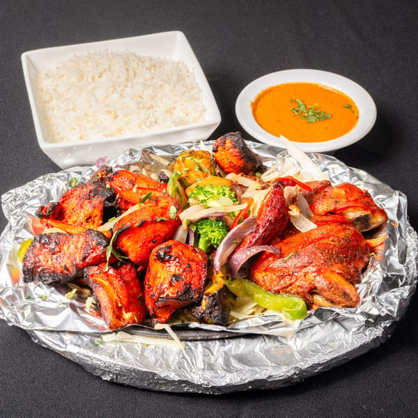 Saffron Indian Cuisine's Tandoori Chicken, rice, and orange sauce on a black background.