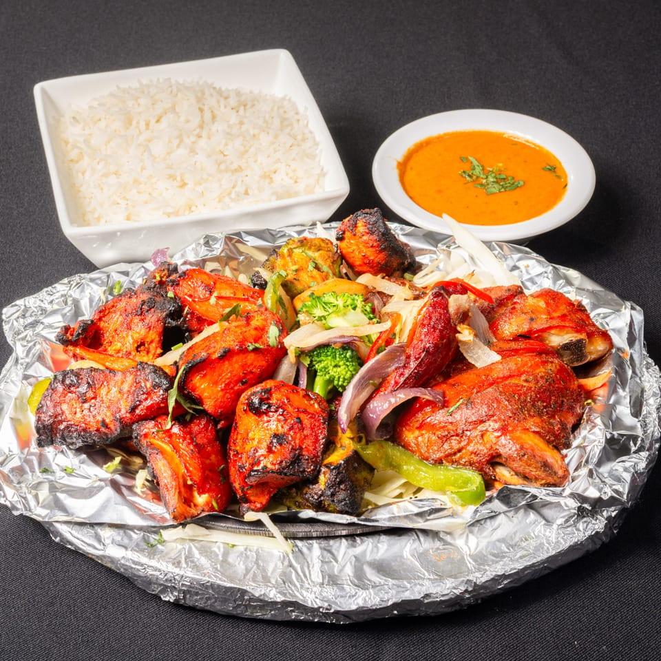 Saffron Indian Cuisine's Tandoori Chicken, rice, and orange sauce on a black background.