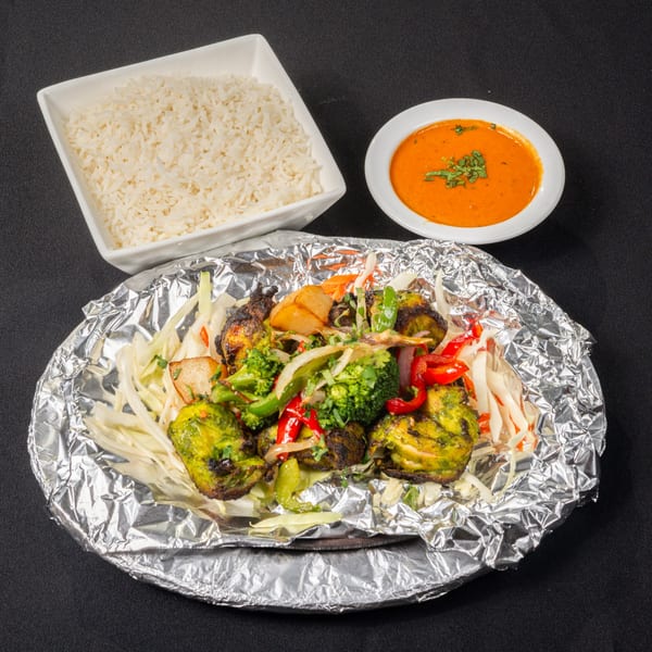 Saffron Indian Cuisine's green chicken tikka with vegetables, rice, and a side of orange curry.