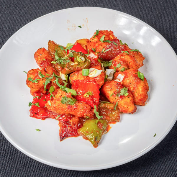 Saffron Indian Cuisine's chili chicken, featuring crispy chicken pieces, bell peppers, and onions in a vibrant red sauce.